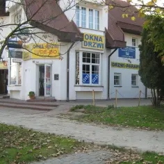 Budynek z żółtymi szyldami "OKNA DRZWI" i "DRZWI PARAPETY" w Olsztynie.