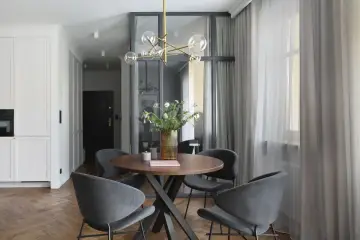Nowoczesna jadalnia z okrągłym stołem, szarymi krzesłami i designerską lampą.
